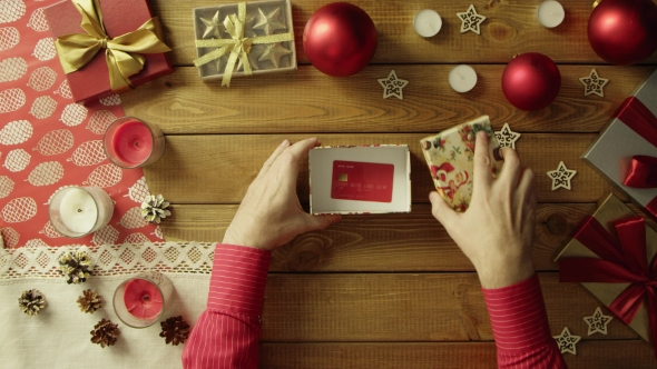 Man Opens Christmas Gift Box with Credit Card Inside, Top Down Shot