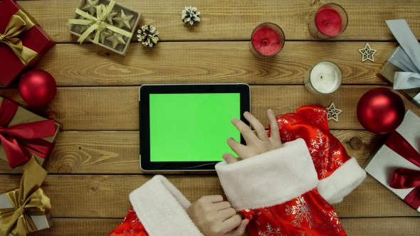 Man in Santa Suit Uses Tablet Pc with Green Screen By New Year Decorated Table, Top Down Shot