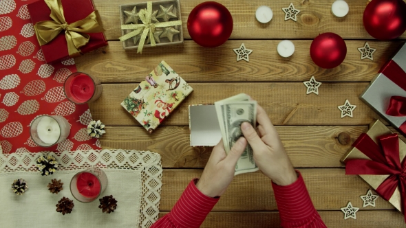 Man Puts Cash Money Into Xmas Present on Wooden Decorated Table, Top Down Shot