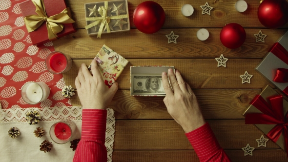 Man Puts Cash Money Into Christmas Gift Box on Wooden Decorated Table, Top Down Shot