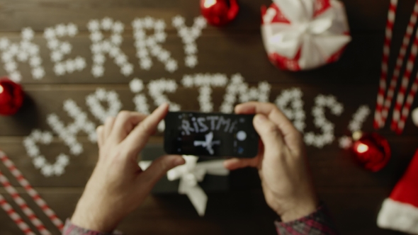 Man Takes Photo of His Christmas Present on Smartphone Camera on Decorated Christmas Table, Top Down