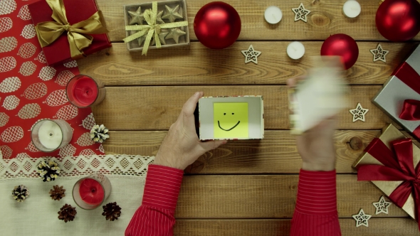 Top Down Shot of Man Opening Christmas Present with Sticky Note with Smile Inside