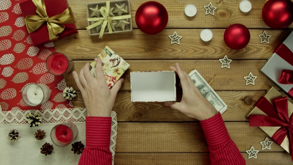 Man Puts Cash Money Into Xmas Present Box on Wooden Decorated Table, Top Down Shot