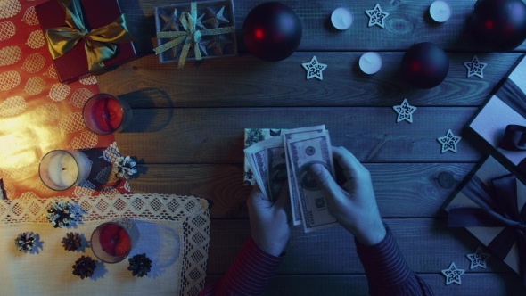 Man Puts Cash Money Into New Year Gift Box on Wooden Decorated Table, Top Down Shot