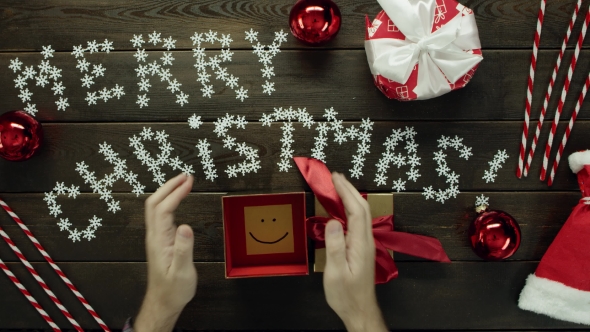 Top Down Shot of Adult Man Opening Christmas Present with Sticky Note with Smile Inside