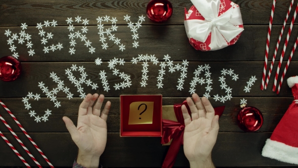 Adult Man Opens Christmas Present with Sticky Note with Question Mark on It, Top Down Shot