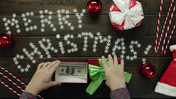 Adult Man Puts Cash Money Into Christmas Present Box on Wooden Decorated Table, Top Down Shot