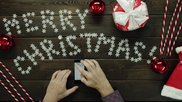 Man with Smartphone Dials Phone Number and Calls While Sitting By Christmas Table, Top Down Shot