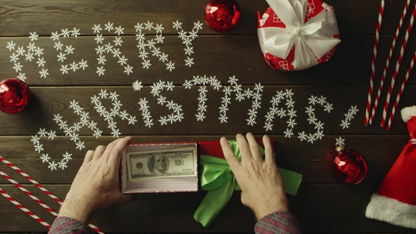 Adult Man Puts Cash Money Into Christmas Gift Box on Wooden Decorated Table, Top Down Shot