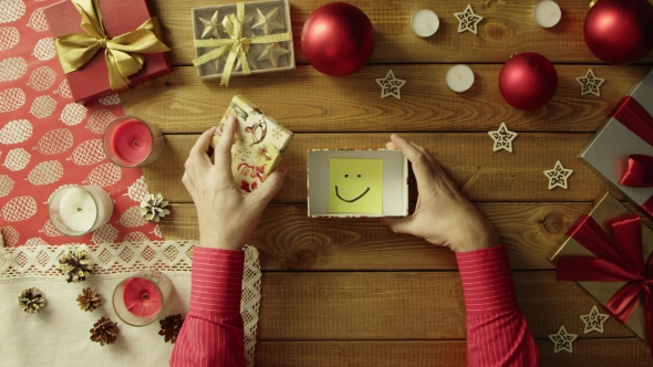 Top Down Shot of Man Opening Christmas Gift Box with Sticky Note with Smile Inside