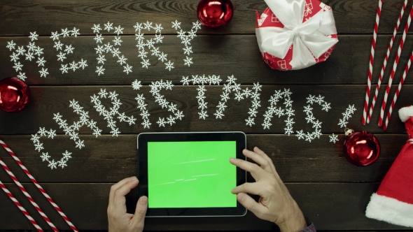 Adult Man Uses Tablet Pc with Green Screen By Christmas Decorated Desk, Top Down Shot