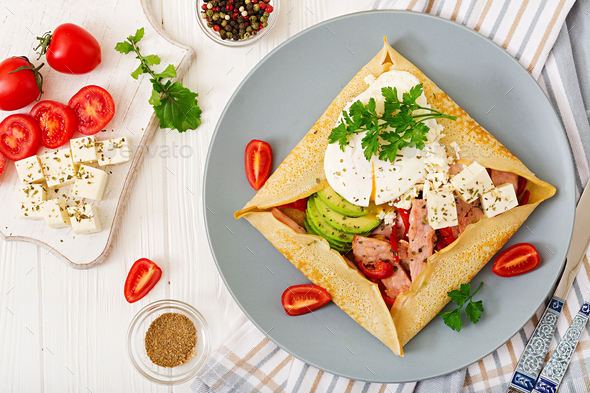 Pancakes with egg poached, feta cheese, fried ham, avocado and tomatoes - Stock Photo - Images
