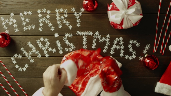 Santa Claus Puts on His Gloves By Wooden Decorated Christmas Table, Top Down Shot