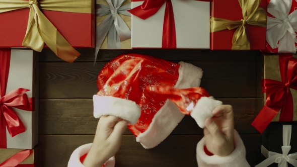 Man in Santa Claus Suit Puts on His Gloves By Wooden Decorated Christmas Table, Top Down Shot