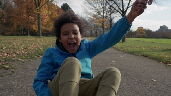 Cute Little Boy with Afro Hair Rides Sitting on Skateboard and Having Fun