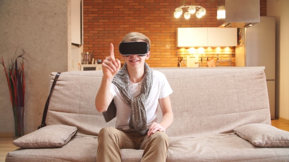 Young Man Uses Virtual Reality Glasses in the House, Leafing Through the Virtual Pages. alt