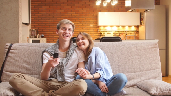 Happy Couple Sitting on the Couch Watching Tv Together at Home in Living Room. alt