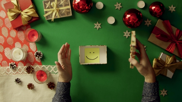 Top Down Shot of Man Opening Christmas Gift Box with Sticky Note with Smile on It Inside on Table