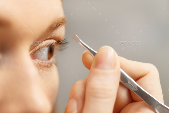 Young Woman Removing Eyebrows Looking At Mirror In Bathroom - Stock Photo - Images