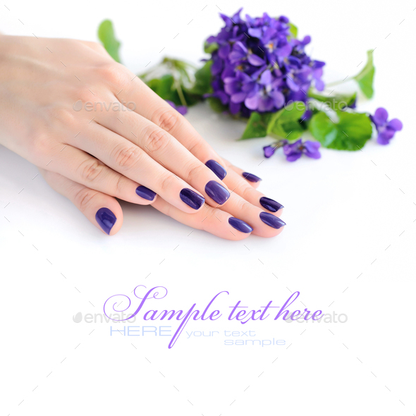 Hands of a woman with violet manicure on nails and flowers viole