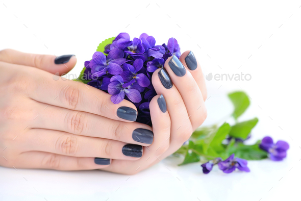 Hands of a woman with dark manicure on nails and bouquet of viol