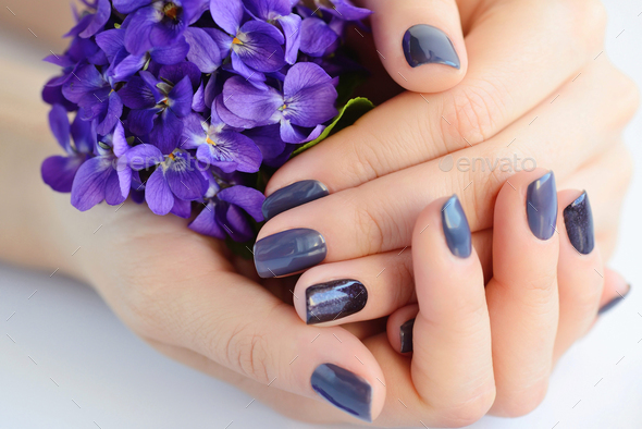 Hands of a woman with dark manicure on nails and flowers violets