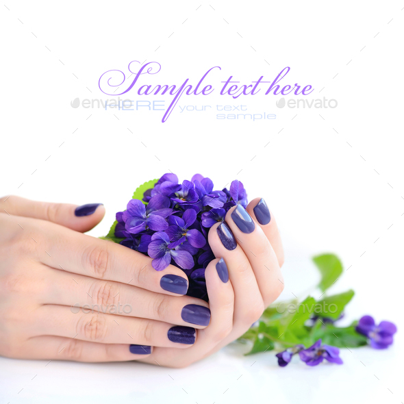Hands of a woman with violet manicure on nails and flowers viole