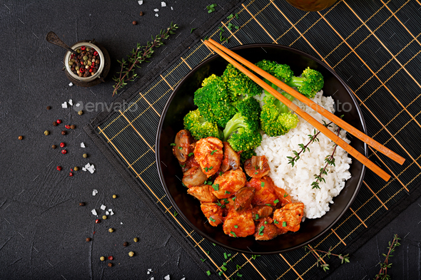 Pieces of chicken fillet with mushrooms stewed in tomato sauce with boiled broccoli and rice Stock Photo by Timolina