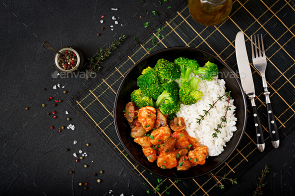 Pieces of chicken fillet with mushrooms stewed in tomato sauce with boiled broccoli and rice.