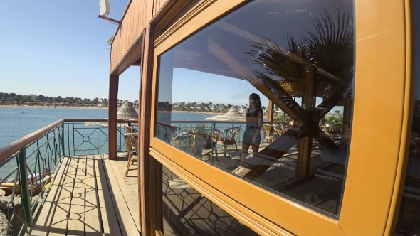 Beautiful Girl Comes out from Behind a Glazed Wall Against the Backdrop of the Lagoon