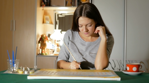 The Girl Draws Her Picture That Lies on the Table and Takes a Break To Drink Tea. Evening Leisure