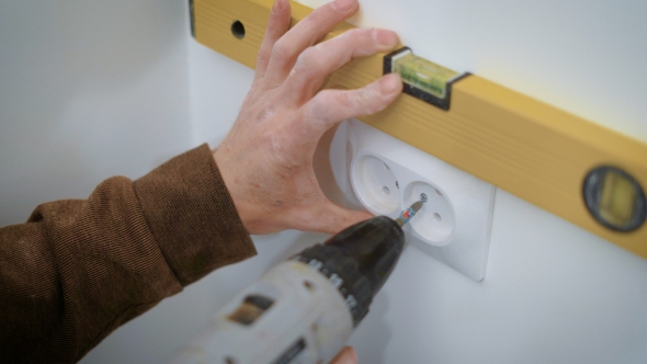 Wireman Is Mounting a Double Socket on a White Wall Inside a Flat, Aligning and Twisting Bolts alt