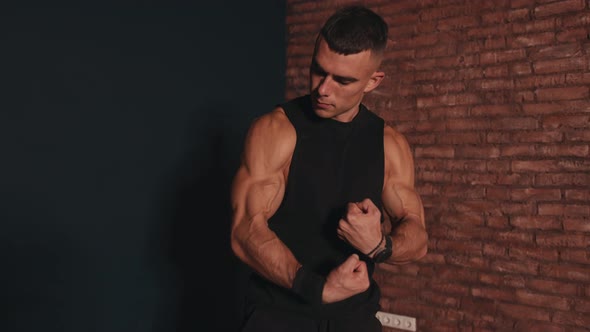 Young Muscular Man in a Black Sleeveless Tshirt Stands Against a Red Brick Wall Background and alt