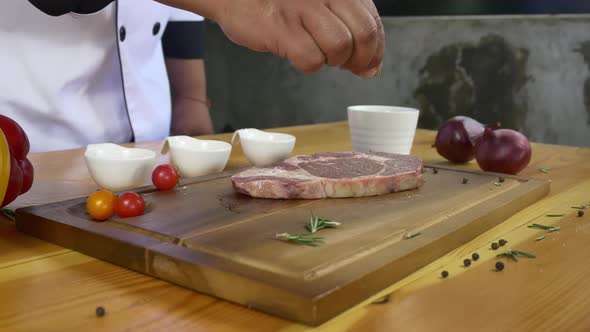 Chef cook season fresh chunk of deli piece of beef with sea salt and grounded spicy peppers.
