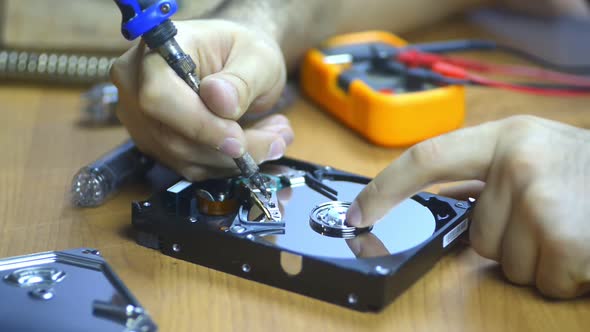 Computer Technician Repairing Hard Drive at Desk with Tools and Electronic Components Technology alt