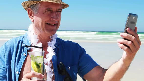 Senior man having video call on the mobile phone at the beach alt