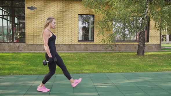 Adult Fitness Woman Doing Walking Lunges with Dumbbells on a Sports Ground