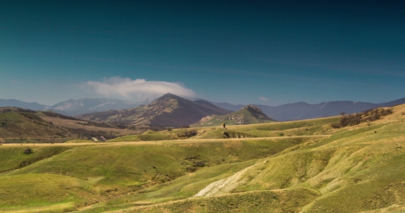 White Clouds Float Above Green Hills and Rocky Mountains