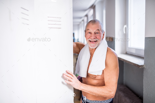 Senior man standing by the lockers in an indoor swimming pool. Stock Photo by halfpoint