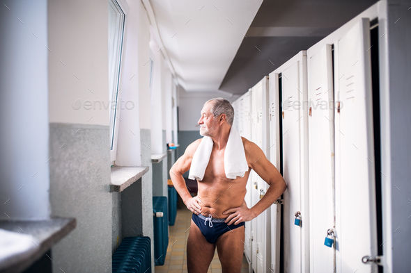 Senior man standing by the lockers in an indoor swimming pool. Stock Photo by halfpoint