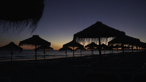 Sunset on the Beach with Silhouettes of the Straw Umbrellas Against the Sky.