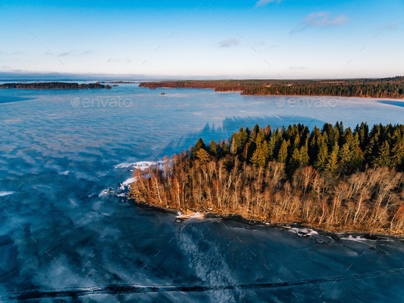 Aerial view of the winter snow forest and frozen lake from above captured with a drone in Finland. Stock Photo by nblxer