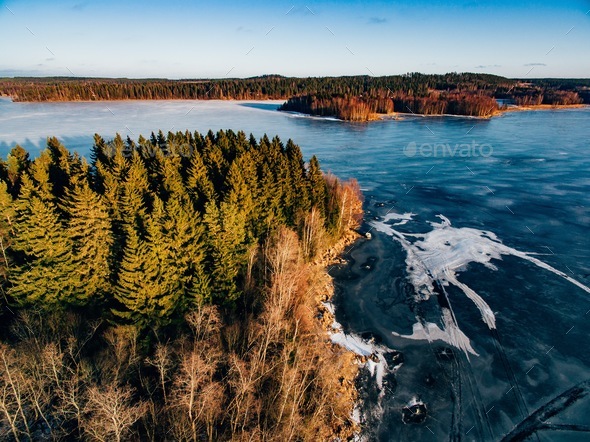 Aerial view of the winter snow forest and frozen lake from above captured with a drone in Finland. Stock Photo by nblxer