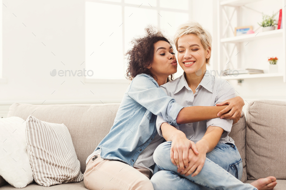 Young woman kissing her friend on the cheek Stock Photo by Milkosx