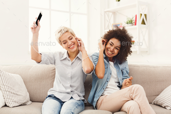 Two women listening music and sharing earphones Stock Photo by Milkosx
