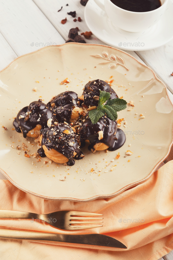 French profitroles with chocolate icing and mint leaves Stock Photo by Milkosx