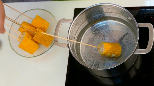 Hands Move Corn on a Stick of Pan