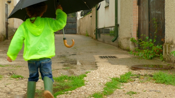Boy with an Umbrella Running Around the Yard in Rubber Boots