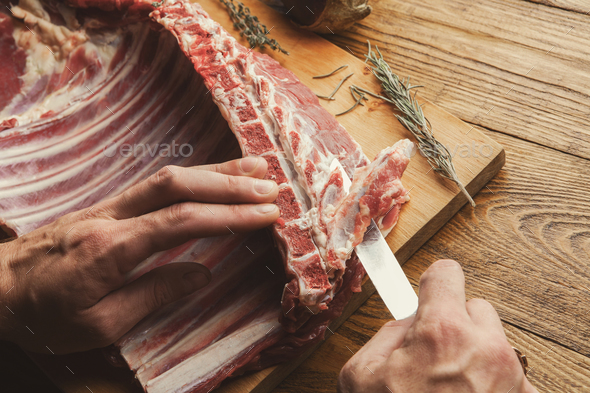 Chef cutting rack of lamb on wooden board in kitchen - Stock Photo - Images