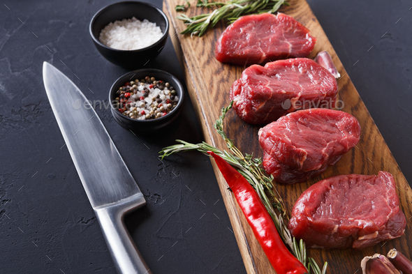 Filet mignon steaks and spices on wood at black background - Stock Photo - Images